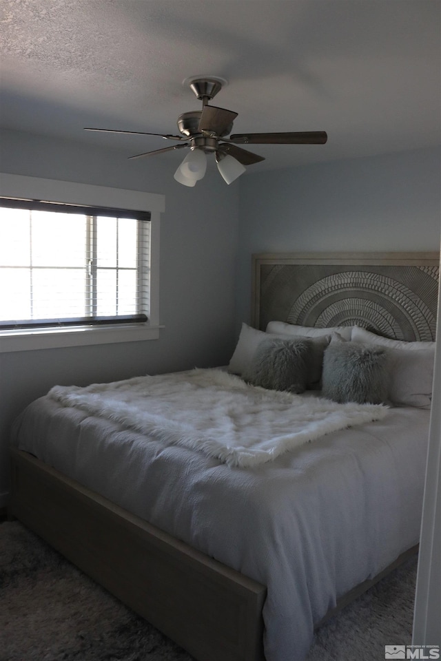 carpeted bedroom featuring ceiling fan and a textured ceiling