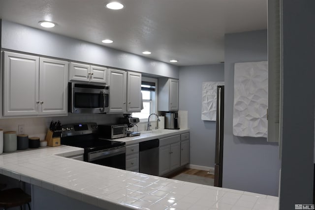 kitchen with tasteful backsplash, wood-type flooring, sink, tile countertops, and stainless steel appliances