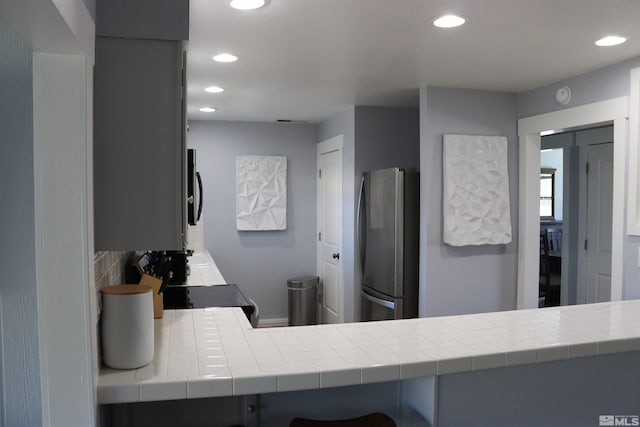 kitchen with kitchen peninsula, tasteful backsplash, appliances with stainless steel finishes, tile countertops, and gray cabinetry