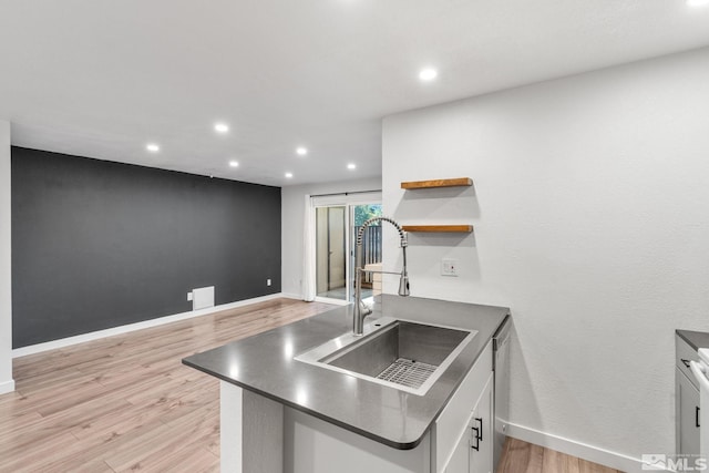 kitchen with kitchen peninsula, sink, light wood-type flooring, stainless steel dishwasher, and white cabinets