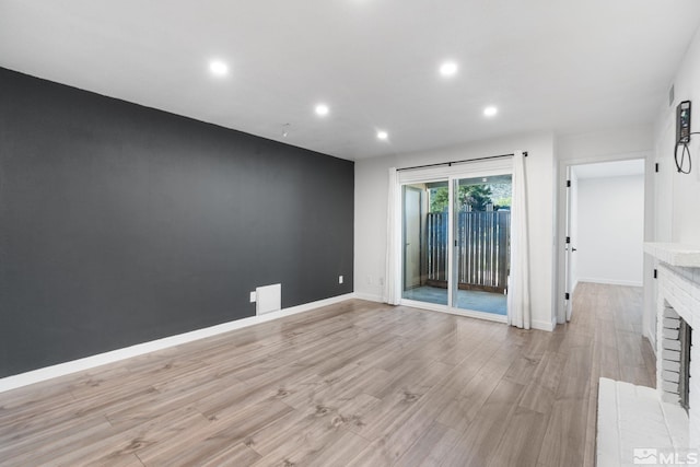 empty room with light hardwood / wood-style floors and a brick fireplace