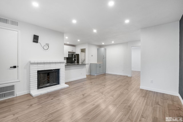 unfurnished living room featuring light wood-type flooring and a brick fireplace