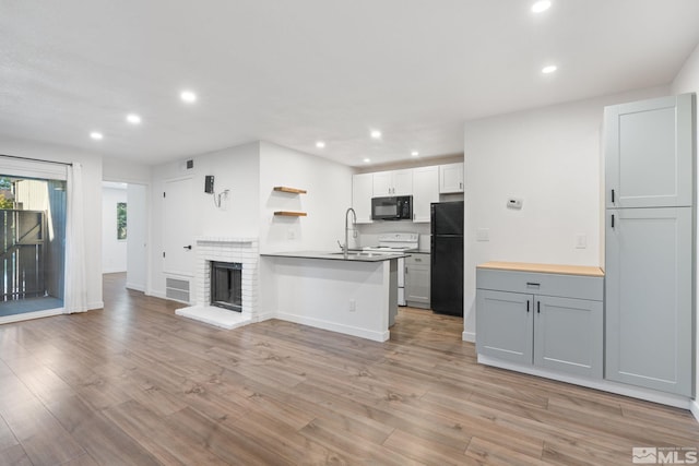 kitchen with white cabinets, black appliances, light wood-type flooring, a brick fireplace, and gray cabinets