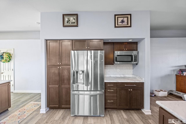 kitchen with decorative backsplash, appliances with stainless steel finishes, light stone countertops, dark brown cabinets, and light hardwood / wood-style floors