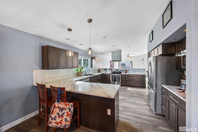 kitchen with kitchen peninsula, a kitchen bar, light wood-type flooring, stainless steel appliances, and hanging light fixtures