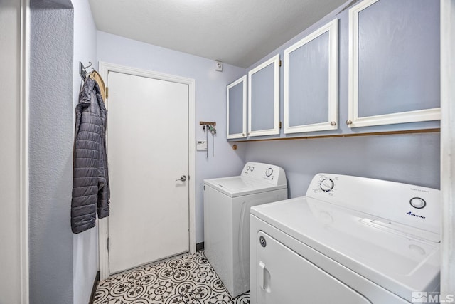 laundry room with washing machine and clothes dryer, cabinets, and a textured ceiling