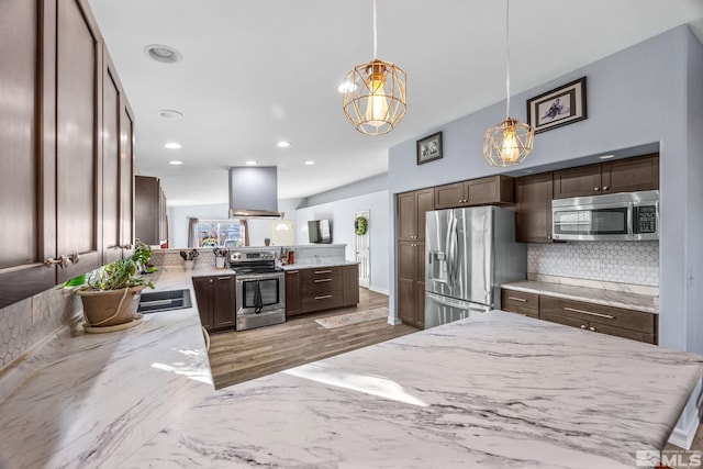 kitchen with pendant lighting, wall chimney range hood, kitchen peninsula, appliances with stainless steel finishes, and dark brown cabinetry