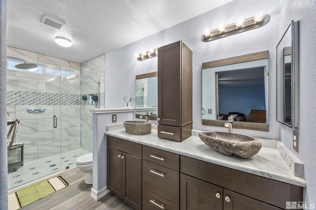 bathroom featuring wood-type flooring, a textured ceiling, toilet, a shower with door, and vanity