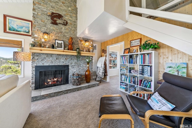 interior space with wooden walls, a stone fireplace, high vaulted ceiling, and carpet