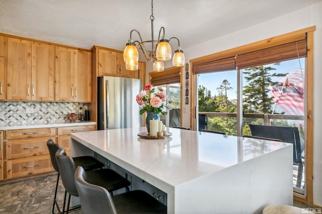 kitchen featuring backsplash, an inviting chandelier, stainless steel refrigerator, decorative light fixtures, and a center island