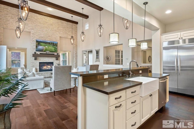 kitchen with a high ceiling, sink, white cabinetry, appliances with stainless steel finishes, and a fireplace