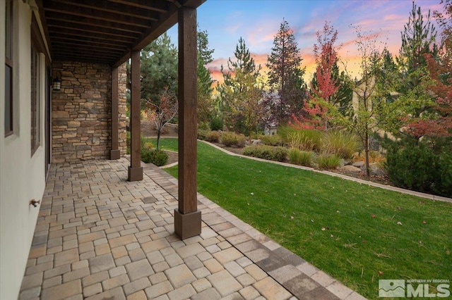 patio terrace at dusk featuring a lawn