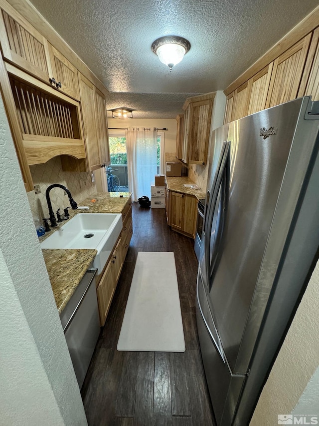 kitchen featuring decorative backsplash, a textured ceiling, light brown cabinetry, dark wood-type flooring, and stainless steel appliances