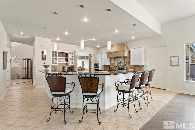 kitchen featuring tasteful backsplash, built in fridge, custom exhaust hood, white cabinets, and a breakfast bar area