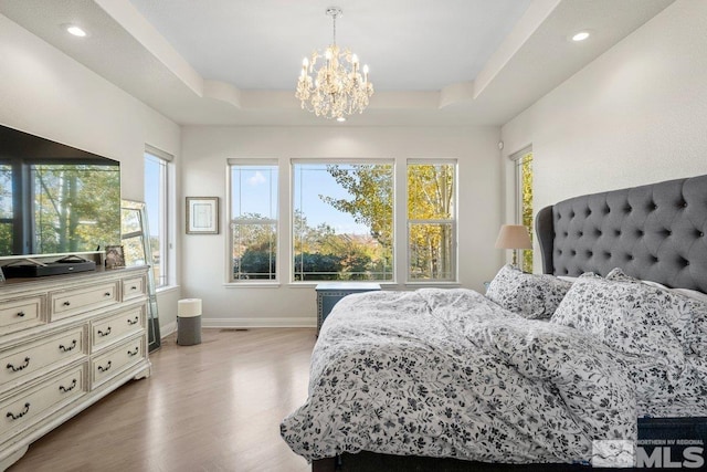 bedroom featuring a notable chandelier, light wood-type flooring, and a raised ceiling