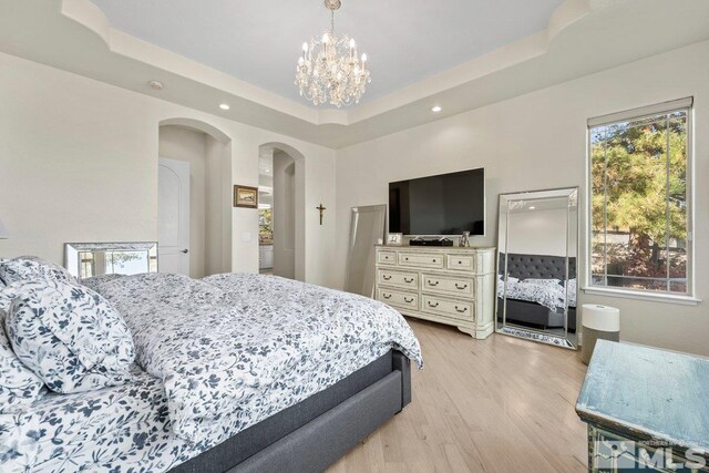 bedroom with a chandelier, a tray ceiling, and light wood-type flooring