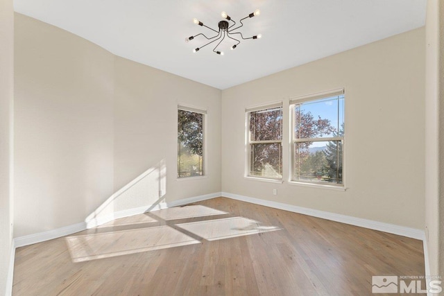 spare room with a notable chandelier and light wood-type flooring