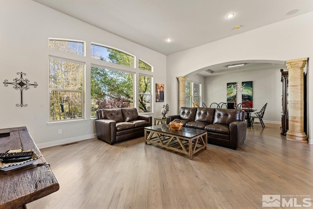 living room featuring ornate columns, lofted ceiling, and light wood-type flooring