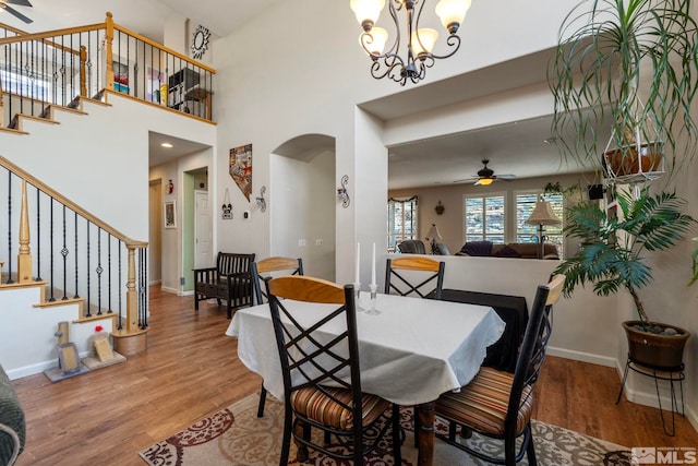 dining space with a towering ceiling, hardwood / wood-style flooring, and ceiling fan with notable chandelier