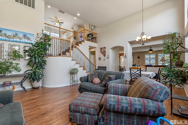 living room with wood-type flooring, a high ceiling, and ceiling fan with notable chandelier