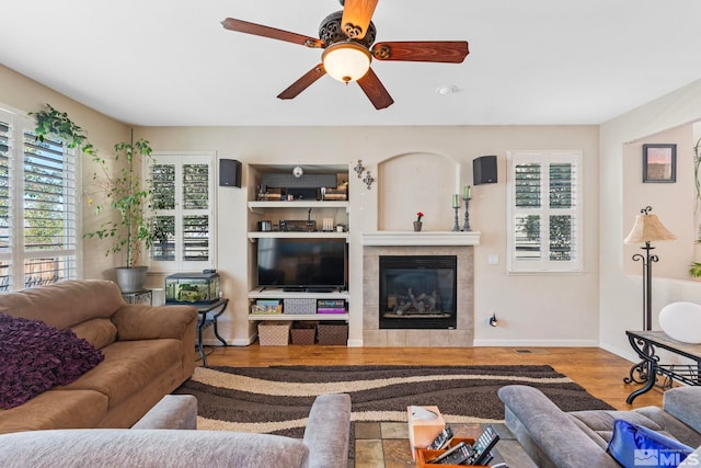 living room featuring ceiling fan, a tiled fireplace, and hardwood / wood-style floors