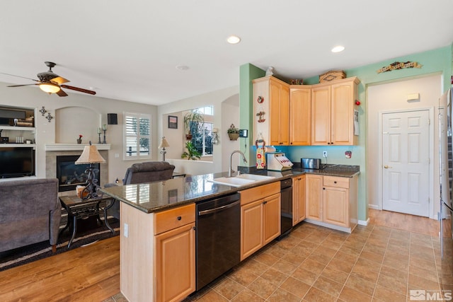 kitchen with kitchen peninsula, black dishwasher, light hardwood / wood-style flooring, a tile fireplace, and sink