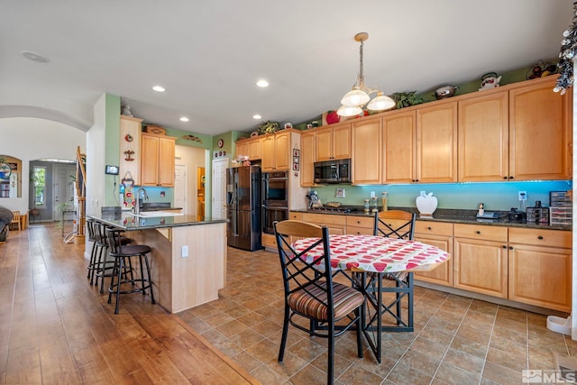 kitchen with hanging light fixtures, stainless steel appliances, light wood-type flooring, and dark stone counters