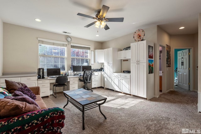 living room with built in desk, light carpet, and ceiling fan