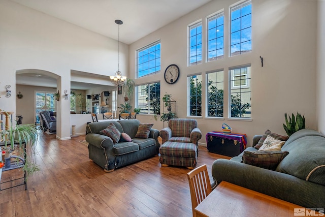 living room with a notable chandelier, hardwood / wood-style flooring, and a towering ceiling