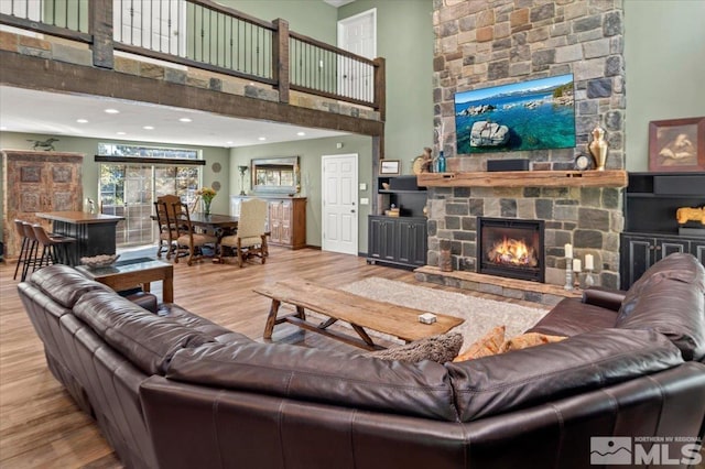 living room with a towering ceiling, a stone fireplace, and light hardwood / wood-style floors