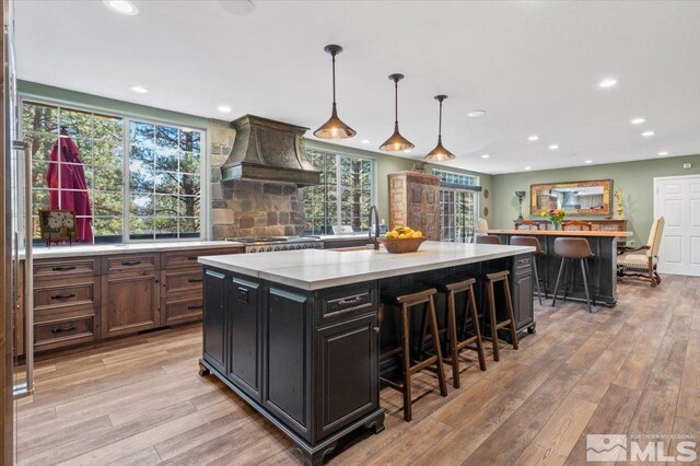 kitchen with custom range hood, a breakfast bar, a center island, pendant lighting, and light wood-type flooring