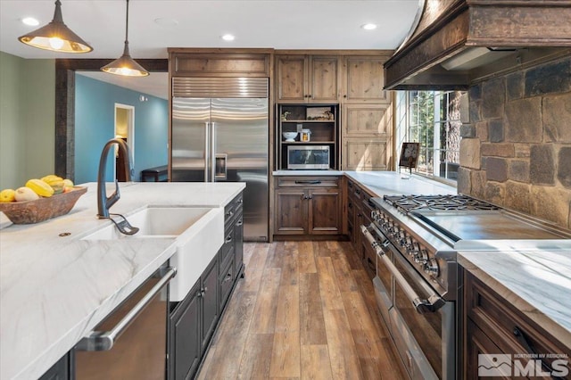 kitchen featuring high quality appliances, hardwood / wood-style floors, pendant lighting, custom exhaust hood, and light stone counters