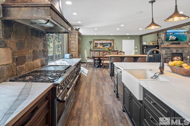 kitchen featuring high end stainless steel range, dark hardwood / wood-style floors, sink, a stone fireplace, and decorative light fixtures