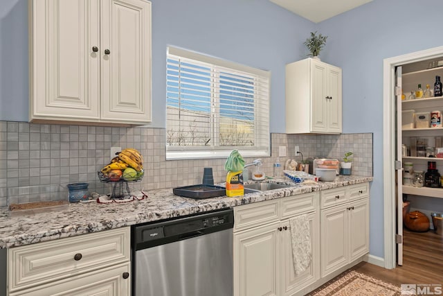 kitchen with stainless steel dishwasher, backsplash, sink, and light stone counters