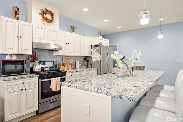 kitchen with a kitchen bar, stainless steel appliances, decorative backsplash, hanging light fixtures, and a center island