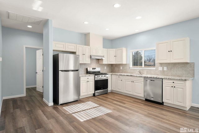 kitchen featuring white cabinetry, hardwood / wood-style flooring, appliances with stainless steel finishes, light stone countertops, and sink