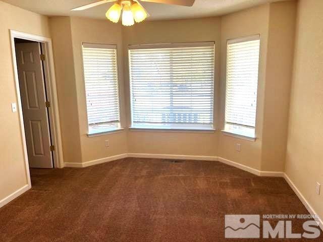 empty room with ceiling fan and dark colored carpet