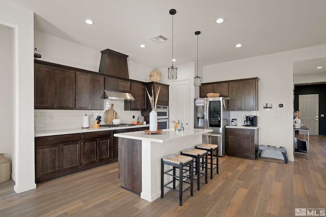 kitchen featuring dark wood-type flooring, hanging light fixtures, appliances with stainless steel finishes, and a kitchen island with sink