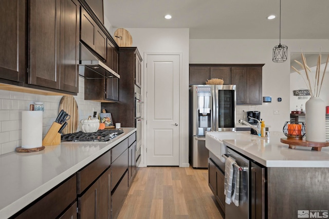 kitchen featuring tasteful backsplash, sink, hanging light fixtures, stainless steel appliances, and light hardwood / wood-style flooring