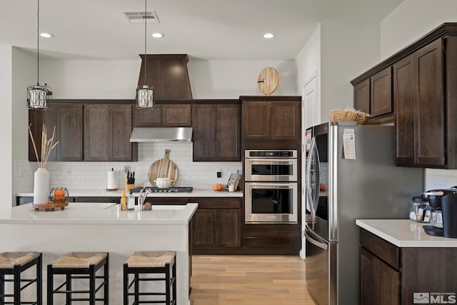 kitchen featuring decorative backsplash, dark brown cabinets, pendant lighting, light wood-type flooring, and appliances with stainless steel finishes