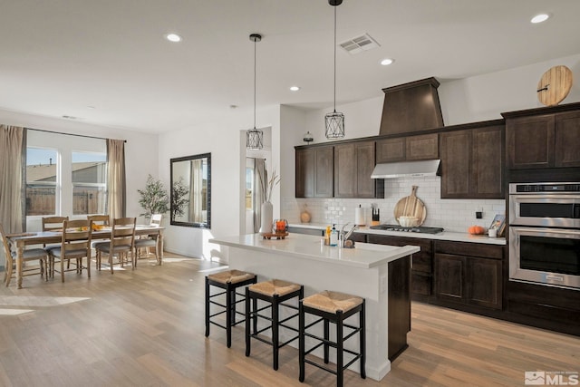 kitchen featuring stainless steel appliances, light hardwood / wood-style flooring, pendant lighting, and a center island with sink