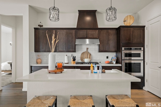 kitchen with a kitchen island with sink, appliances with stainless steel finishes, light wood-type flooring, and hanging light fixtures