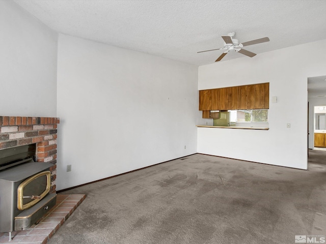 unfurnished living room featuring a wood stove, ceiling fan, carpet, and a textured ceiling