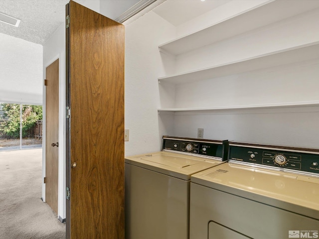 clothes washing area featuring washing machine and clothes dryer, light carpet, and a textured ceiling