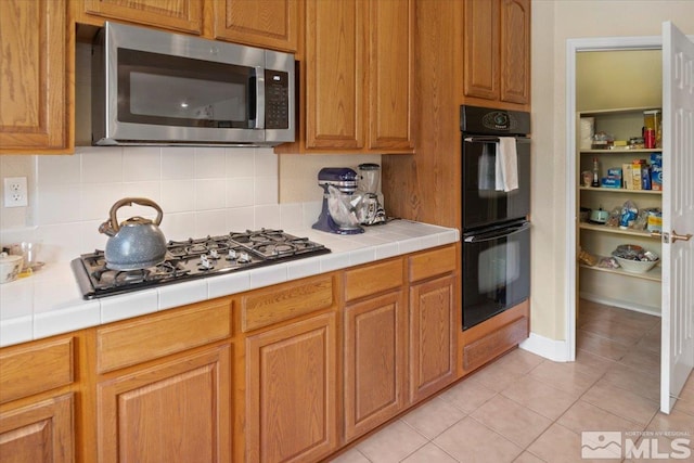 kitchen featuring light tile patterned floors, double oven, gas stovetop, and tile counters