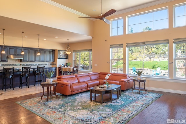 living room featuring crown molding, a towering ceiling, dark hardwood / wood-style floors, and ceiling fan