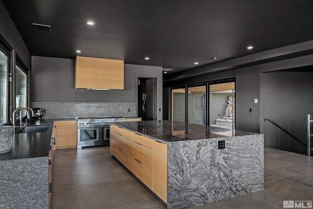 kitchen with a kitchen island, light brown cabinets, dark stone counters, sink, and double oven range