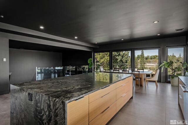 kitchen with a spacious island, light brown cabinets, and dark stone counters