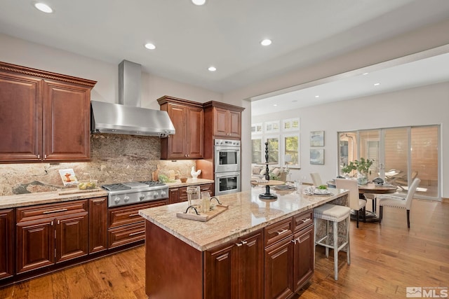 kitchen with tasteful backsplash, stainless steel appliances, light hardwood / wood-style floors, wall chimney exhaust hood, and a center island