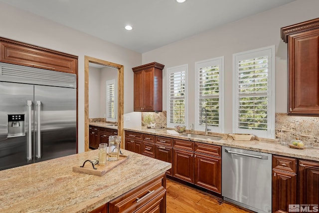 kitchen featuring light stone countertops, stainless steel appliances, light hardwood / wood-style floors, and tasteful backsplash